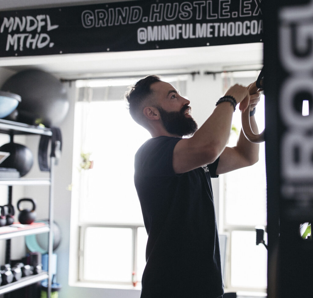 coach mike doing ring setup with grind and hustle written on the wall behind him. in a gym and black shirt